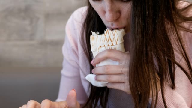 Mujer-irreconocible-comer-danar-o-Shawarma-sentado-en-un-café-y-escribiendo-un-mensaje-en-el-teléfono-móvil.