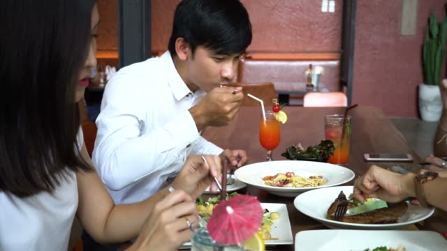 Grupo-de-cuatro-jóvenes-asiáticos,-un-hombre,-tres-mujeres,-comiendo-y-hablando-en-la-cafetería-y-restaurante.-Concepto-de-la-amistad