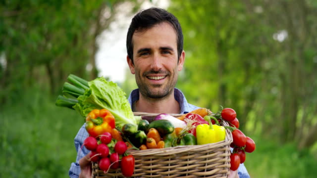Porträt-eines-glücklichen-jungen-Landwirts-mit-frischem-Gemüse-in-einen-Korb.-Auf-Grund-der-Natur.