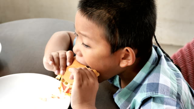 Cute-asian-boy-are-happy-eating-a-hamburger-in-restaurant.-Video-4k-Slow-motion