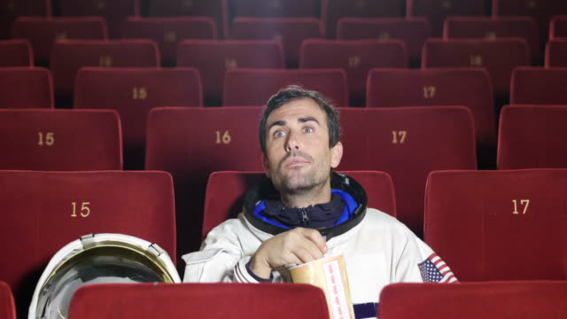 Un-astronauta-de-la-película-mira-una-película-comiendo-palomitas-de-maíz-y-disfrutar-la-película.-Concepto-de:-películas-de-cine-y-espacio,-película-de-otras-situaciones-del-mundo,-surrealistas.