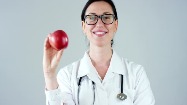 portrait-of-a-nutritionist,-an-expert-on-food-and-health-welfare,-smiles-looking-into-camera-and-holding-an-apple-on-a-white-background.