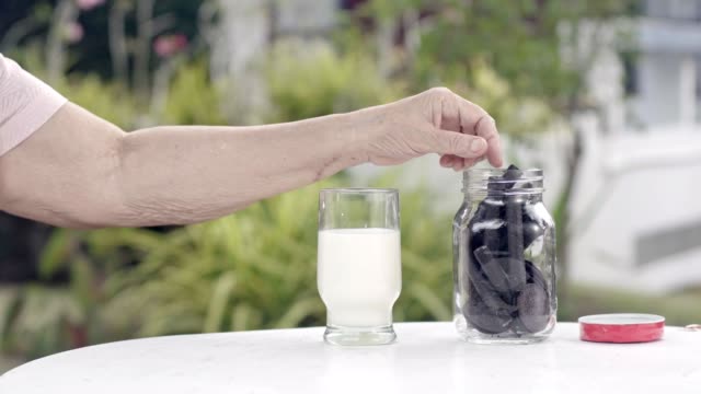 ältere-Menschen-hand-eintauchen-und-eine-Schoko-Cookie-In-Glas-Milch-rühren