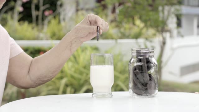 elderly-hand-dipping-and-stir-a-chocolate-cookie-In-milk-glass