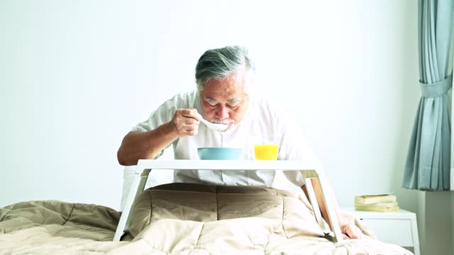 Älteren-Mann-im-Bett-gefrühstückt.-Alten-asiatischen-Mann-mit-weißem-Bart-Essen-Congee-und-Orangensaft.-Senior-home-Service-Konzept.