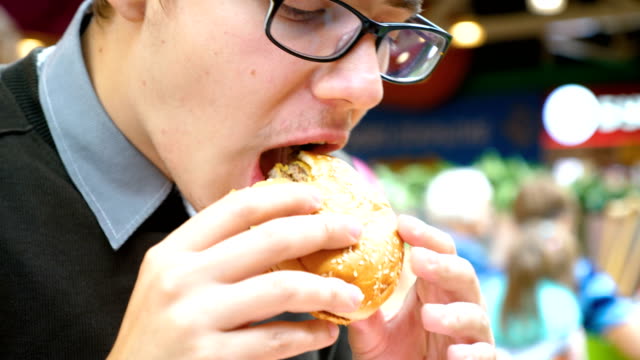 A-young-man-is-eating-a-hamburger-in-a-shopping-center.