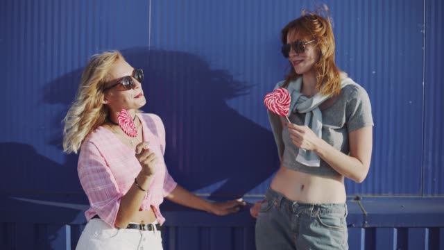 Two-young-attractive-women--walking--and-talking-on-street-and-eat-lollipop