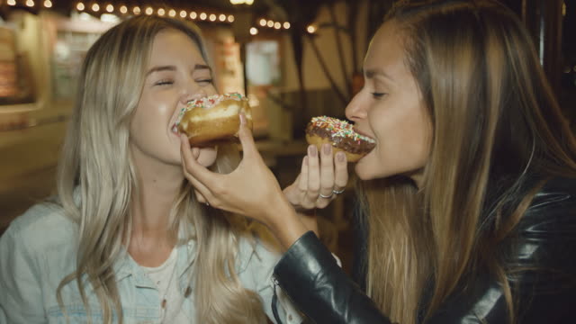 Two-cute-girls-having-fun-eating-donuts-smiling-with-silly-faces