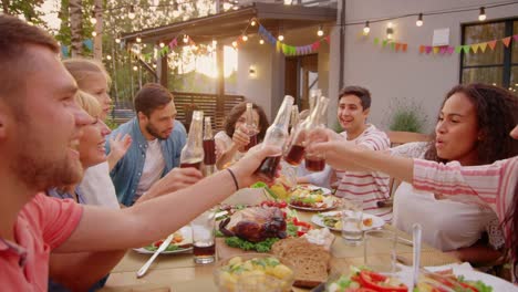 Family-and-Friends-Gathered-Together-at-the-Table-Raise-Glasses-and-Bottles-To-Make-a-Toast-and-Clink-Glasses.-Big-Family-Garden-Party-Celebration.