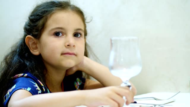 Porträt,-Nahaufnahme,-ziemlich-Kid-Girl,-lockige-Brünette-zappelt-beim-Sitzen-an-einem-Tisch-in-einem-restaurant