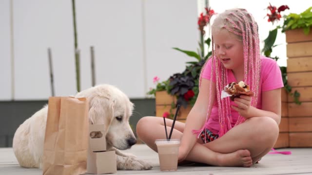 Liebe-für-Haustiere---schöne-Mode-Mädchen-mit-afrikanischen-Zöpfen-isst-auf-der-Straße-mit-ihrem-Hund