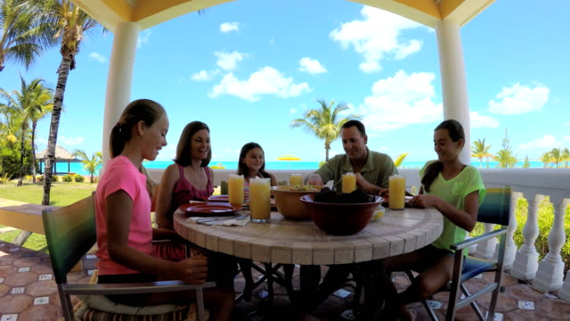 Caucasian-family-dining-on-vacation-beach-hotel-decking