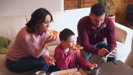 Familie-mit-Hilfe-von-digital-Tablette-während-des-Essens-Pizza-im-Wohnzimmer
