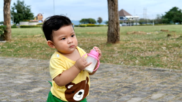 Niño-Asiático-caminando-y-sosteniendo-una-botella-de-leche-en-el-parque-al-aire-libre