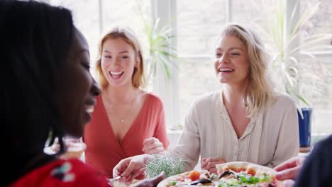 Two-young-adult-white-women-eating-lunch-with-friends-at-a-restaurant,-over-shoulder-view,-close-up