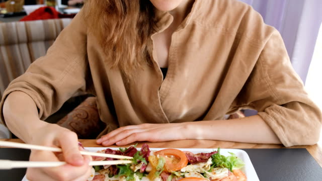Young-beautiful-girl-with-blue-eyes-eating-salad-with-raw-fish-sticks-in-a-restaurant
