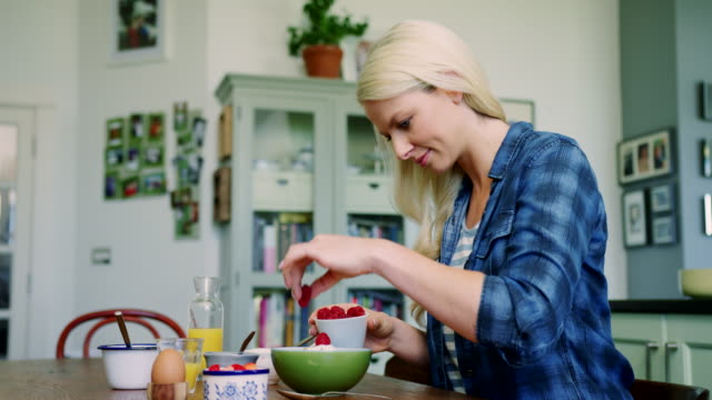 Beautiful-Blond-Woman-Adding-Raspberries-And-Honey-To-Granola