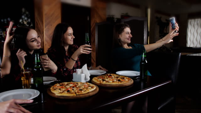 La-compañía-de-chicas-alegres-en-la-pizzería.-Chica-haciendo-un-selfie-con-un-smartphone-en-la-pizzería.