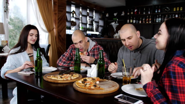 Spaß-im-Restaurant-Pizza-essen-und-Bier-zu-trinken.-Zwei-Jungs-und-zwei-Mädchen-in-der-Pizzeria.