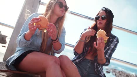 Teen-Mädchen-Essen-Burger-zusammen-im-Freien-an-einem-sonnigen-Tag