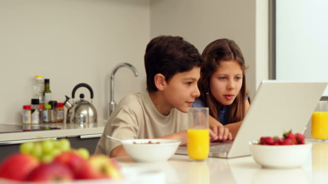 Niedliche-Geschwister-mit-laptop-beim-Frühstück