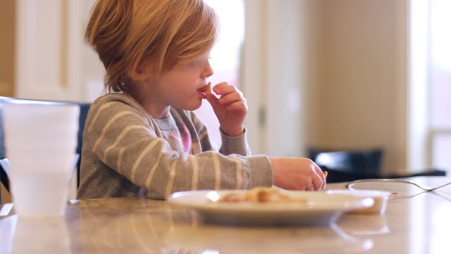 A-little-girl-eating-crackers-at-the-kitchen-counter,-slow-motion
