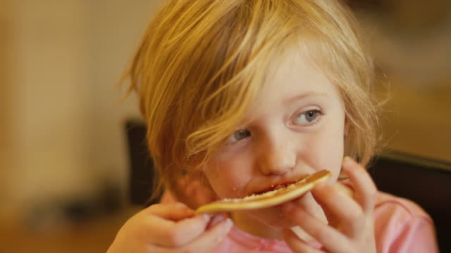 A-little-girl-eating-a-pancake-with-her-hands,-close-up,-slow-motion