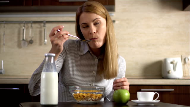 Beautiful-young-attractive-businesswoman-eating-cornflakes-for-breakfast-in-kitchen.-Cup-of-coffee