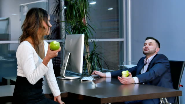 Dos-empleados-de-oficina-tiene-una-rotura,-aeting-verdes-manzanas-y-hablando-en-la-oficina