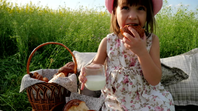 Fin-de-semana-en-picnic,-niña-en-la-pradera-de-flores-con-pasteles-y-la-leche,-niño-alegre-feliz,-hermosa-chica-en-Prado-de-la-flor-con-la-cesta