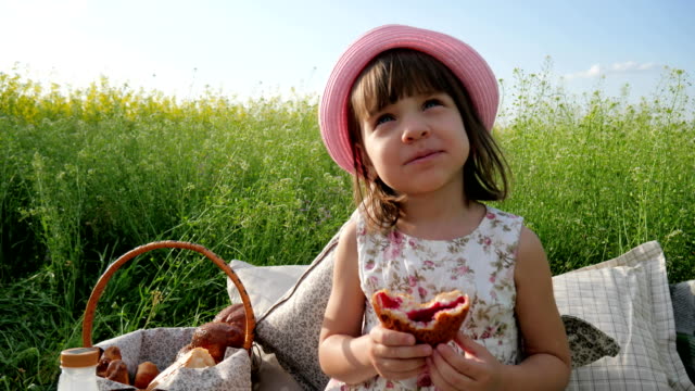 female-child-in-panama-with-bun-on-nature,-Weekend-at-picnic,-Girl-on-flower-meadow-with-pastries-and-milk,-Happy-joyful-child
