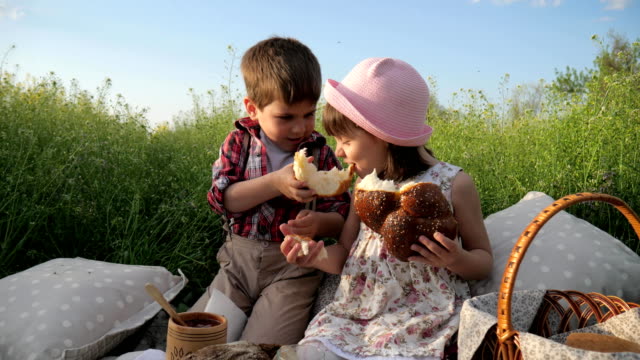 niño-alimenta-a-chica-con-productos-de-panadería,-lindos-niños-pequeños-compartir-pan,-productos-de-baske-de-picnic,-los-niños-divirtiéndose-en-el-aire-fresco