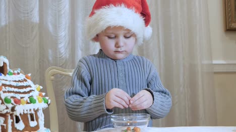 Cute-little-boy-in-santa's-hat-eats-a-chocolate-candy-at-the-kitchen
