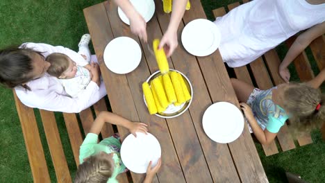 Top-view-of-family-enjoying-an-outdoor-dinner-eating-boiled-corn-on-the-cob