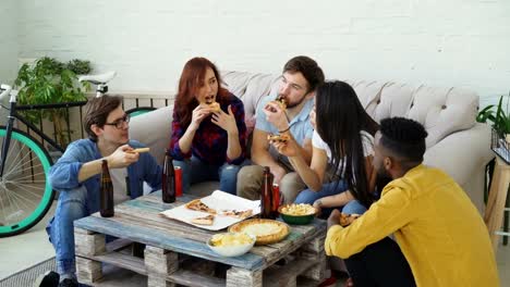 Group-of-young-friends-having-home-party-and-eating-pizza-taking-it-from-table.-Students-talking-and-have-fun