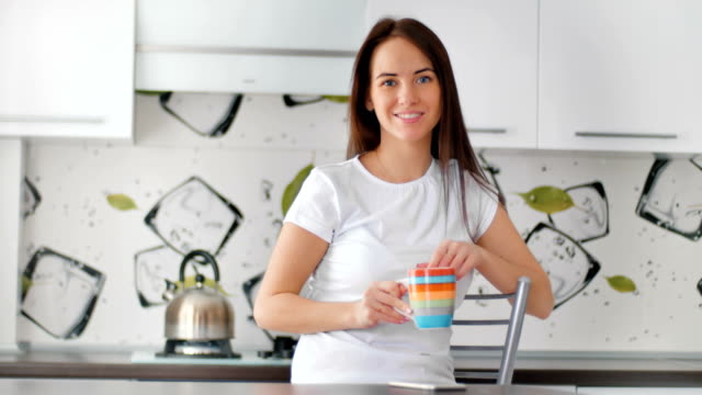 Lächelnde-junge-Frau-mit-Tasse-Tee-posiert-in-der-Küche