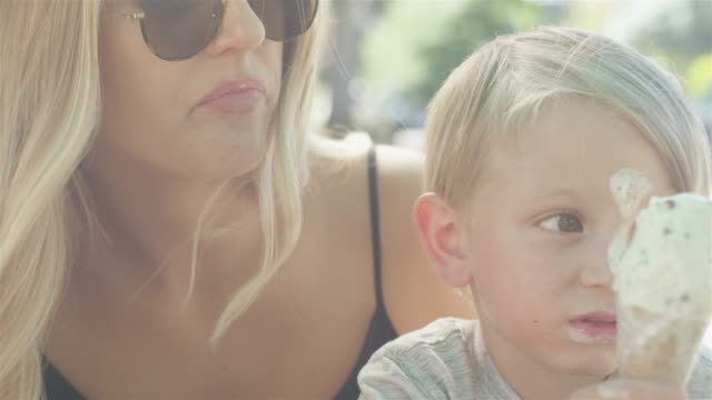 Little-kid-accidentally-shoves-an-ice-cream-cone-on-his-face,-and-laughs-out-loud-with-his-mother-at-the-park