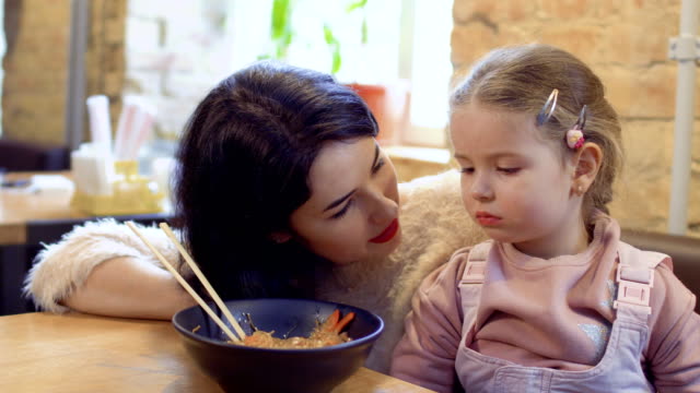 Young-woman-urges-her-little-daughter-to-try-a-korean-delicious-noodles