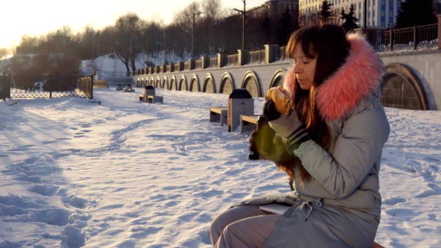 Young-woman-eats-a-burger-on-winter-street