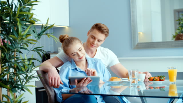 Junges-Paar-mit-digital-Tablette-beim-Frühstück-am-Küchentisch.