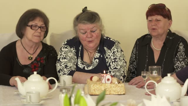 Ältere-Frau-mit-Freundinnen,-die-herumsitzen-und-Esstisch-mit-Geburtstagstorte