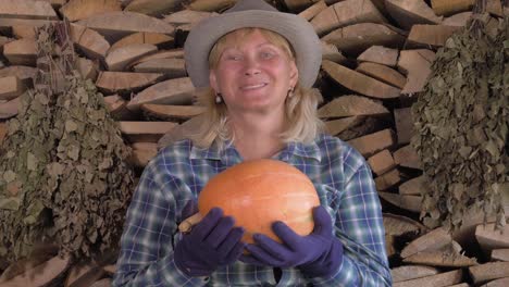 Portrait-Of-Woman-Farmer-On-The-Background-Of-Firewood-Is-Holding-A-Ripe-Pumpkin