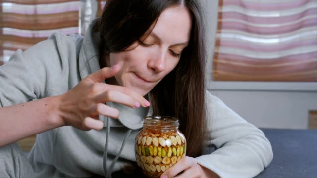 Woman-dips-her-finger-in-honey-with-nuts-in-the-jar.-Eats-honey-from-finger.