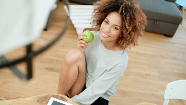 Young-woman-holding-green-apple-while-sitting-at-home.