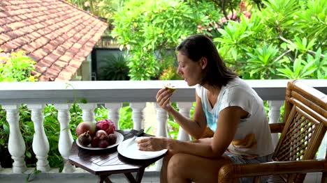 Frau-sitzt-auf-dem-Balkon-und-isst-Passionsfrucht