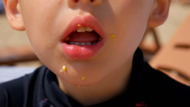 Niño-hambriento-comiendo-maíz-en-la-playa-del-mar.-Se-centran-en-el-maíz-hervido.-Close-up.