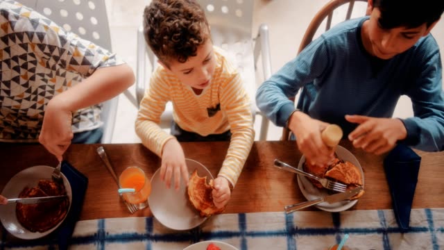Niños-sentados-a-la-mesa-de-la-cocina-y-desayunando-juntos