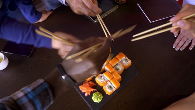 Un-set-de-sushi-rollos-sobre-una-mesa-en-un-restaurante.-Un-grupo-de-amigos-comiendo-sushi-rollos-con-palillos-de-bambú.