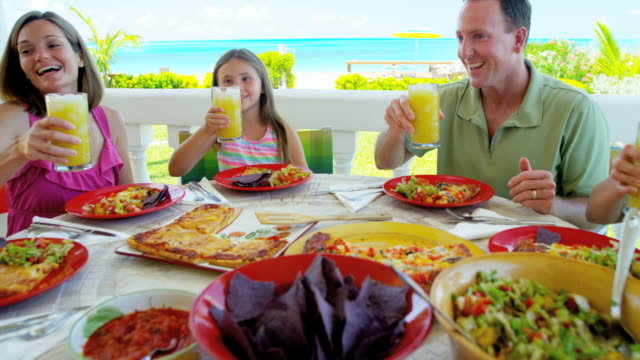 Caucasian-family-eating-lunch-outdoors-on-beach-decking