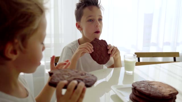 Two-boy-eating-homemade-chocolate-cookies-with-milk-at-kitchen